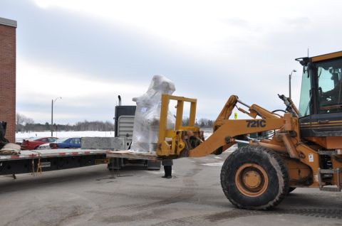1996 Ford Bronco - Construction equipment is used to load a large, wrapped item onto a flatbed trailer.
