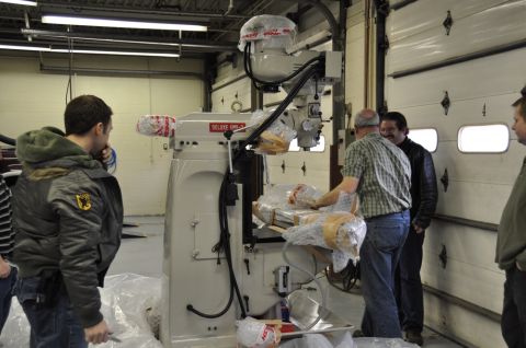 1996 Ford Bronco - A group of men observe a new milling machine, wrapped in protective plastic, inside a garage.