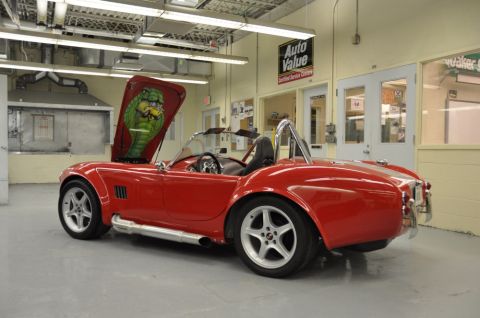 1996 Ford Bronco - A red convertible sports car is parked in a garage with its hood open, revealing custom cobra artwork.