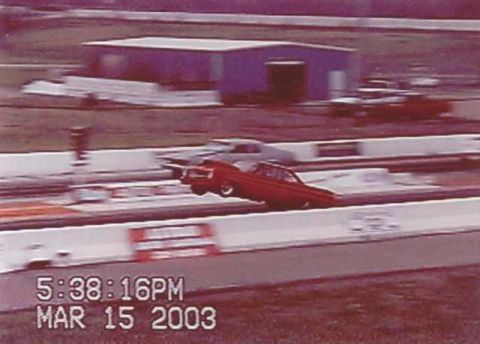 1963 Ford Fairlane - A red car speeds down the drag strip with another vehicle in the background.