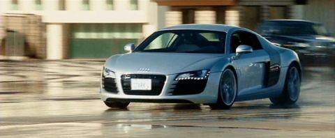 1990 Ford Bronco - A silver Audi R8 sports car is captured in motion on a wet road, with another vehicle blurred in the background.