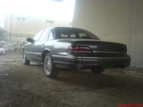 1992 Ford Crown Victoria - Rear three-quarter driver-side view of a dark gray aero Ford Crown Victoria sedan with whitewall tires on wire-spoke wheel covers, parked o…