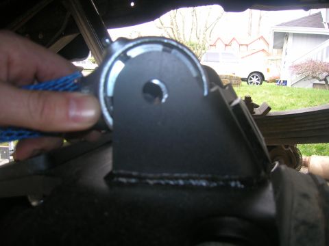 1996 Ford Bronco - A close-up view of a black metal suspension bracket, held by a hand covered in a blue mesh sleeve.