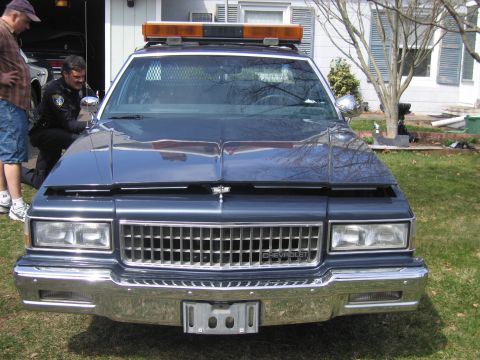 1991 Ford LTD Crown Victoria - Front view of a dark blue police car with its hood open, showing the chrome grille and light bar.