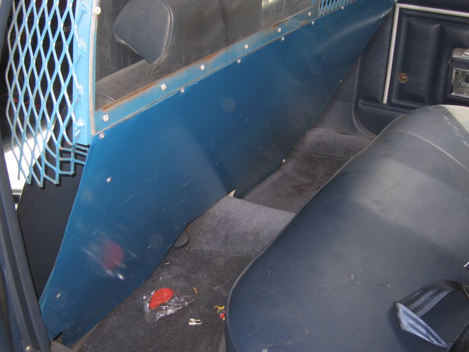Interior of car with blue partition and cage separating front and back seats. Dark blue seats and carpet
