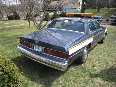 1991 Ford LTD Crown Victoria - This police car, identified as a Caprice by its badging, is seen from the rear. The vehicle features a light bar on the roof and distinctiv…