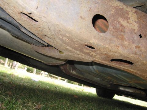 1991 Ford LTD Crown Victoria - The frame of the vehicle shows extensive rust damage and holes, indicating poor condition.