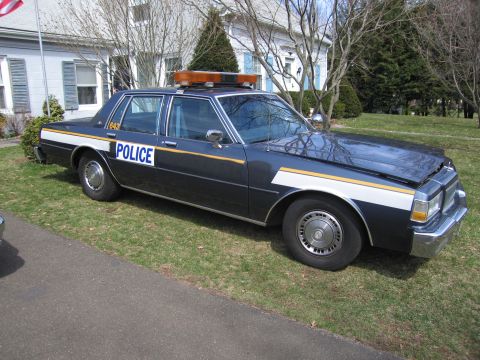 1991 Ford LTD Crown Victoria - This police car, marked with "POLICE" on its side, features a light bar on the roof and distinctive white and yellow stripes along the body.
