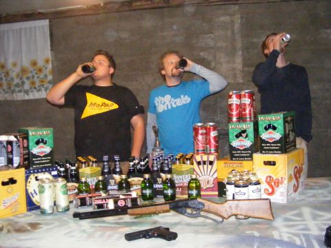 1979 Ford Bronco - A table is laden with beer bottles, cans, and firearms, as three men drink beverages.