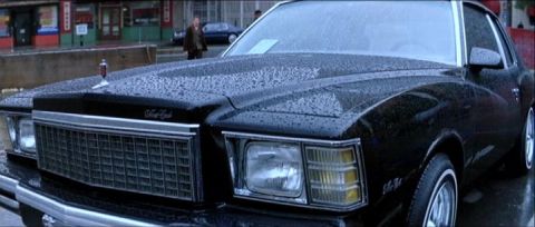 1977 Ford F-100 - A black coupe with a distinctive grille sits on a wet street, with another car visible in the background.
