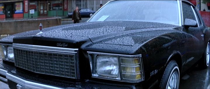 Black coupe with chrome grille and hood ornament, wet from rain. Visible text 'SuperMotors'