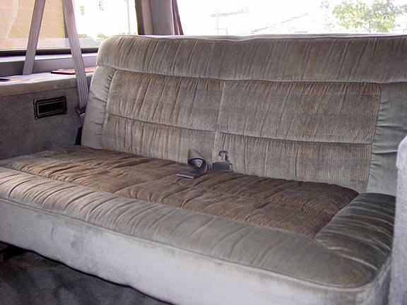 Tan velour bench seat inside a truck or van interior with center seatbelt buckle