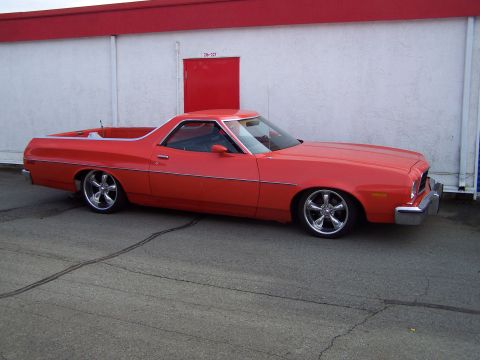 1973 Ford Ranchero - Full passenger-side profile of a red Ford Ranchero coupe utility parked on asphalt in front of a white stucco building with a red door numb…