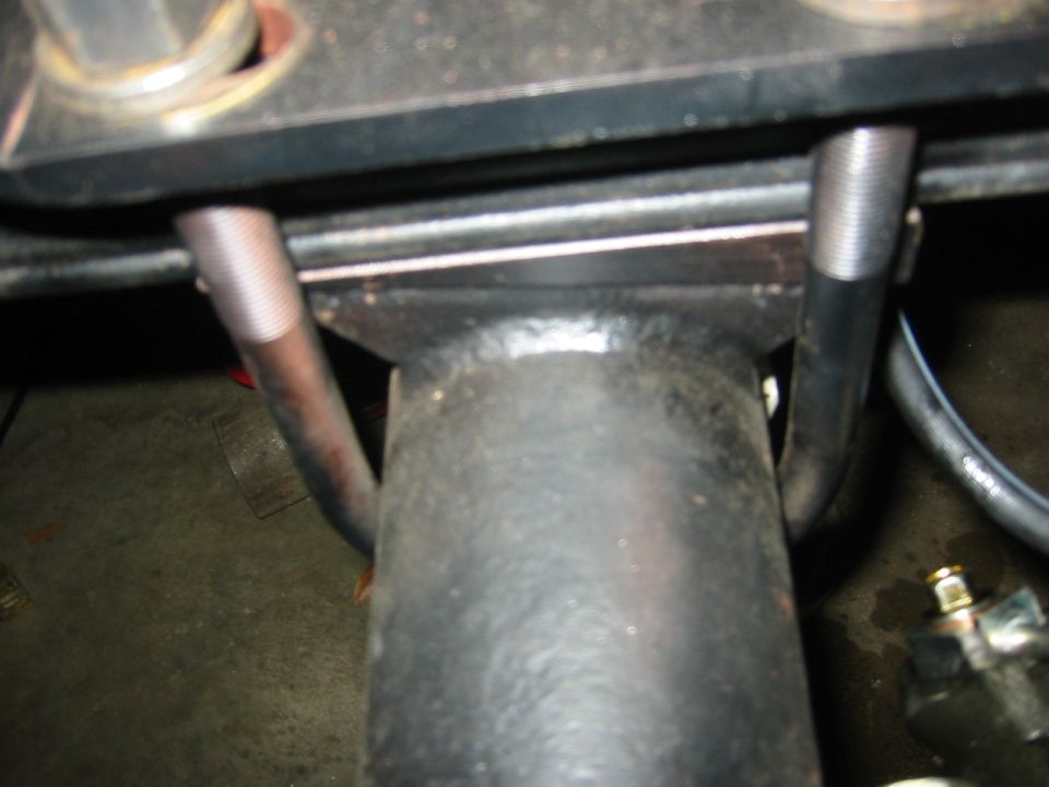 Close-up of a black metal suspension part with threaded bolts and a hose