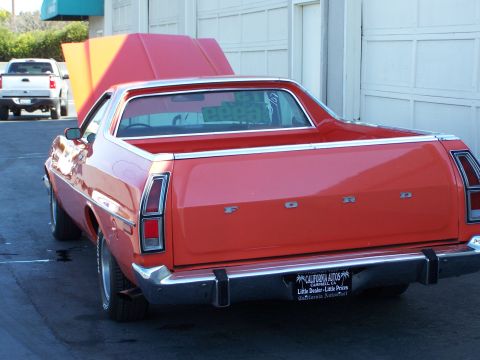 1973 Ford Ranchero - Three-quarter rear view of an orange-red Ford Ranchero coupe-utility parked on asphalt in front of white roll-up garage doors, with FORD bl…