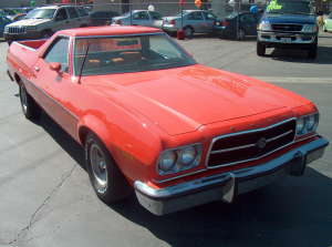 1973 Ford Ranchero - Small, low-resolution three-quarter front view of an orange-red Ford Ranchero coupe-utility parked on a dealer lot, showing its quad headli…