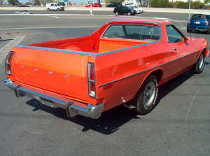 1973 Ford Ranchero - Small, low-resolution three-quarter rear shot of an orange-red Ford Ranchero coupe-utility on an asphalt lot, showing the FORD-lettered tai…