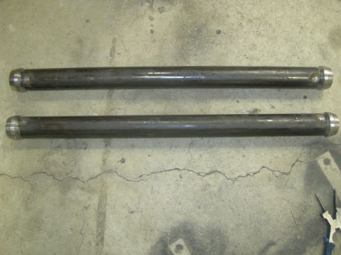 1996 Ford Bronco - Two dark metal suspension rods with silver caps lie on a cracked concrete floor.