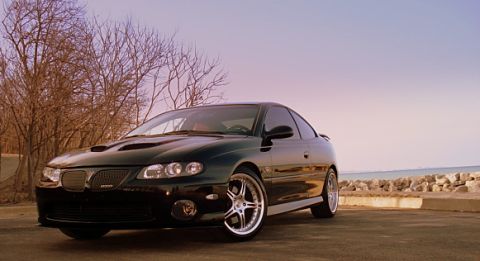 1998 Ford Taurus - A black Pontiac GTO is parked near a rocky shoreline under a clear sky.