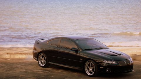 1998 Ford Taurus - Black Pontiac GTO with a prominent hood scoop sits by the water's edge.
