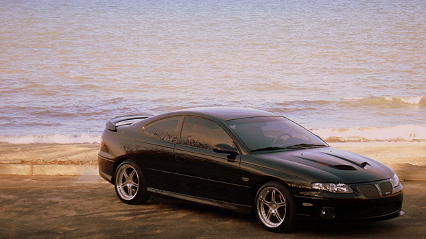 Black Pontiac GTO with hood scoop parked by the ocean