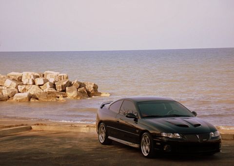 1998 Ford Taurus - Black Pontiac GTO parked by the water with rocks and ocean in the background.