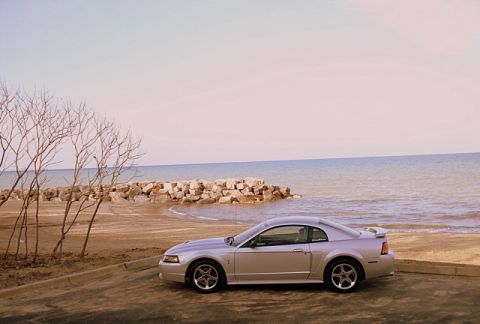 1998 Ford Taurus - A silver coupe is parked on a paved area next to a beach with a rock breakwater.