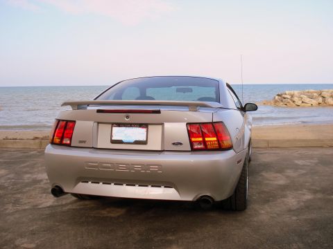 1998 Ford Taurus - The rear of a silver Ford Mustang Cobra is parked near the beach with the ocean in the background.