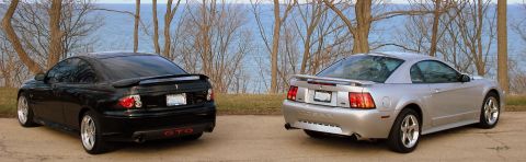 1998 Ford Taurus - Two coupes, a black Pontiac GTO and a silver Ford Mustang, are viewed from the rear with a body of water behind them.