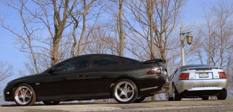 1998 Ford Taurus - Two coupes are parked side-by-side outdoors with bare trees in the background.