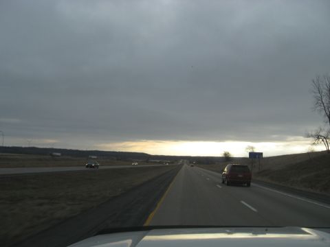1978 Ford Bronco - A red SUV travels down a highway on an overcast day, with other vehicles visible in the distance.