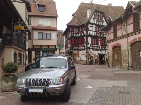 1991 Ford LTD Crown Victoria - Jeep Grand Cherokee parked in a European town square with traditional architecture.