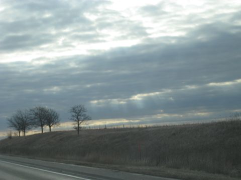 1978 Ford Bronco - Sunlight streams through dramatic clouds over a barren landscape with a few trees on a hill.