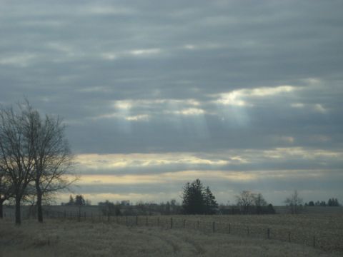 1978 Ford Bronco - Sunbeams pierce through the clouds over a rural landscape with a field and trees.