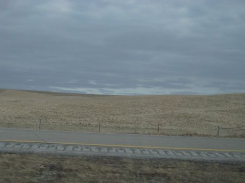 1978 Ford Bronco - A view from a vehicle traveling on a highway next to a harvested field under a cloudy sky.