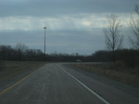 1978 Ford Bronco - A lone white SUV travels down a highway, bordered by bare trees and a tall light pole.
