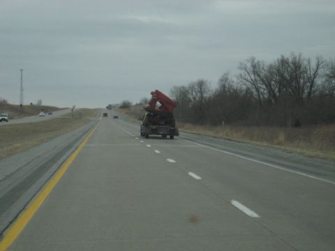 1978 Ford Bronco - A truck transports a large red piece of equipment down a highway under an overcast sky.