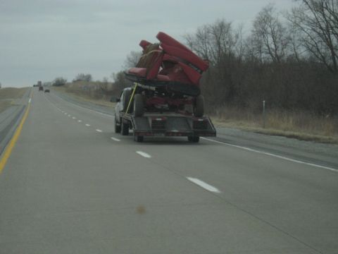 1978 Ford Bronco - Pickup truck transports a red lawn tractor on a flatbed trailer along a highway.