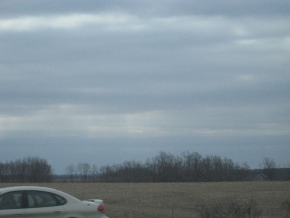 Car driving past a field under a cloudy sky