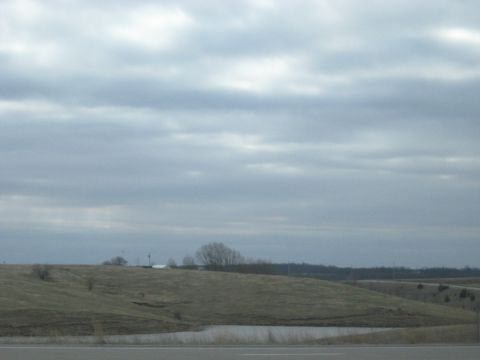 1978 Ford Bronco - A wide landscape shot under a cloudy sky shows rolling hills, a small body of water, and distant trees.