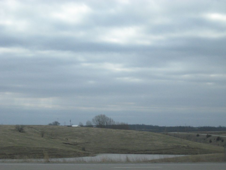Overcast sky above rolling hills and a small pond