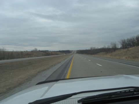 1978 Ford Bronco - Driving on a highway with a cloudy sky overhead, showing the road ahead and the car's hood in the foreground.