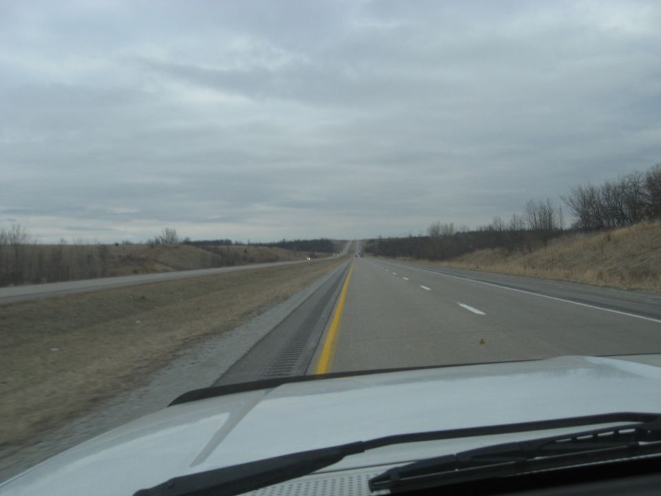View of a highway stretching into the distance under a cloudy sky, seen from the perspective of a car's dashboard