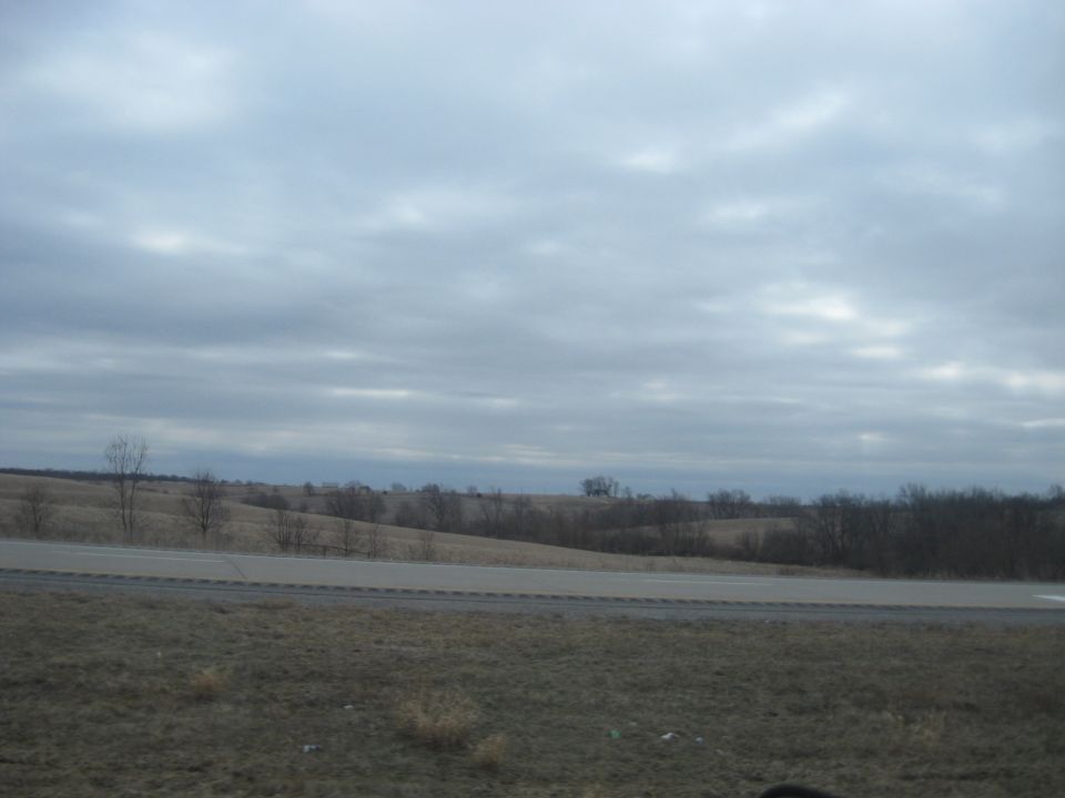 two-lane road runs through a dry, grassy landscape under a cloudy sky