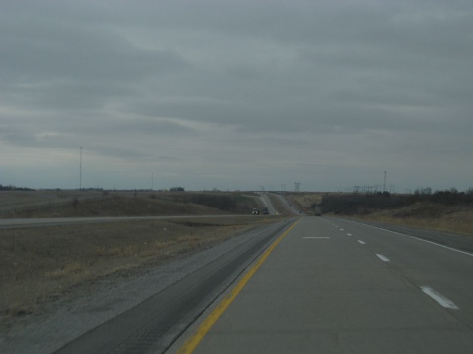 view down a highway with a cloudy sky, some distant cars, and fields on the side