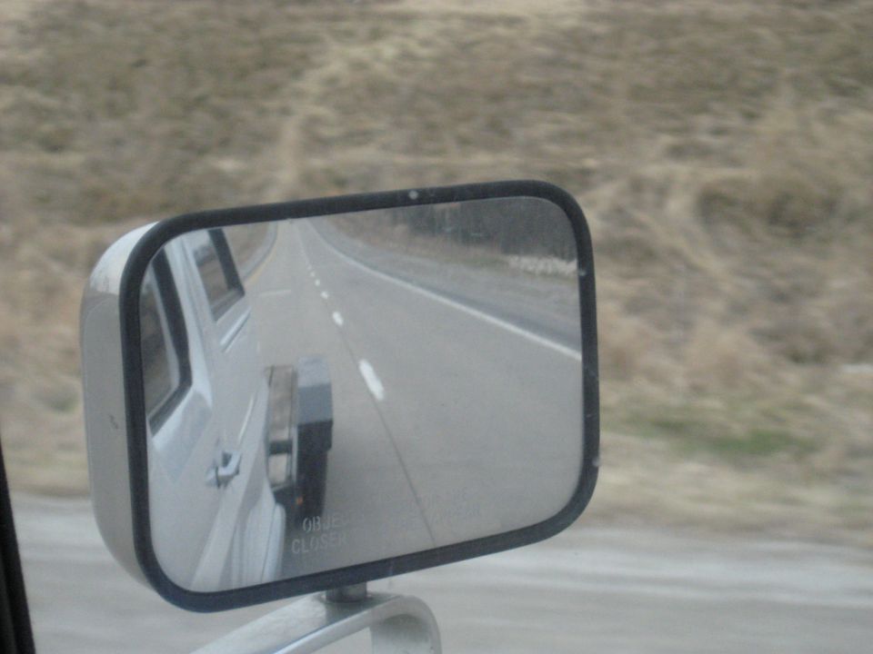Side mirror reflection shows trailer hitch and road ahead