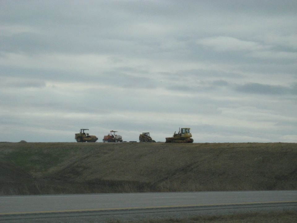Four construction vehicles lined up on a grassy ridge under a cloudy sky