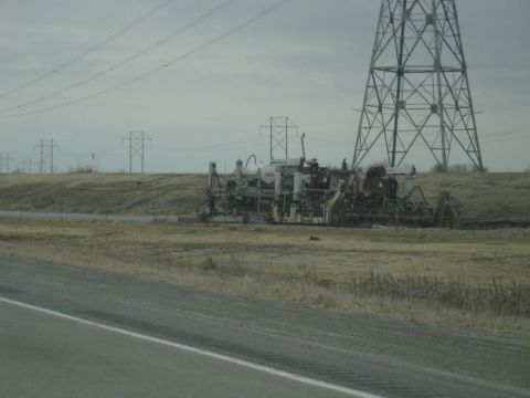 1978 Ford Bronco - Heavy machinery sits idle beside a highway, with tall power line towers dominating the horizon.