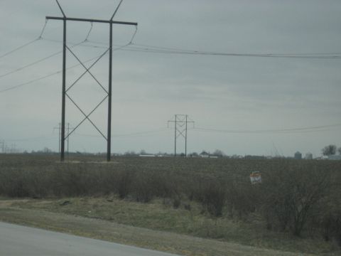 1978 Ford Bronco - Tall power line towers stand in a field with distant farm buildings under an overcast sky.