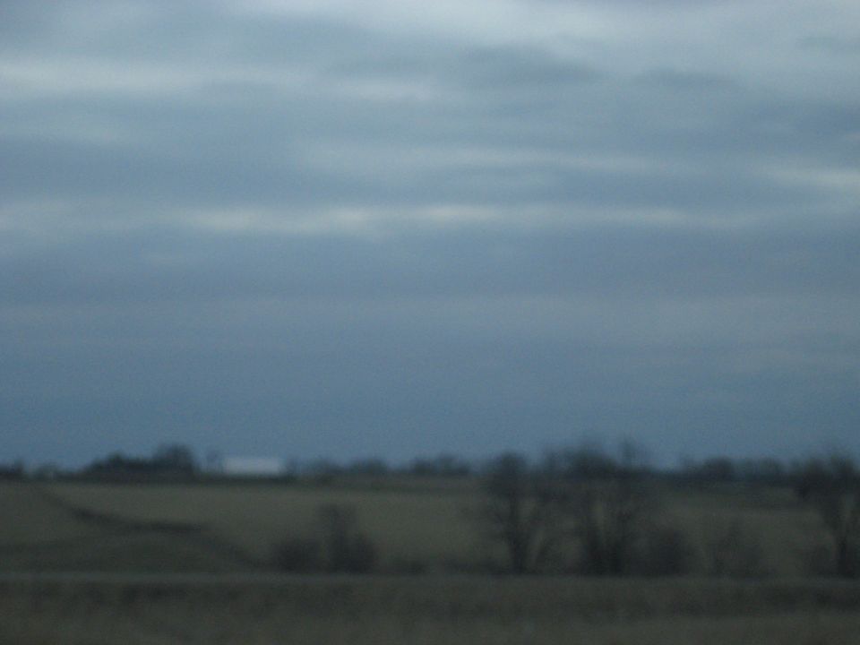 Overcast sky above a blurry rural landscape with trees and fields